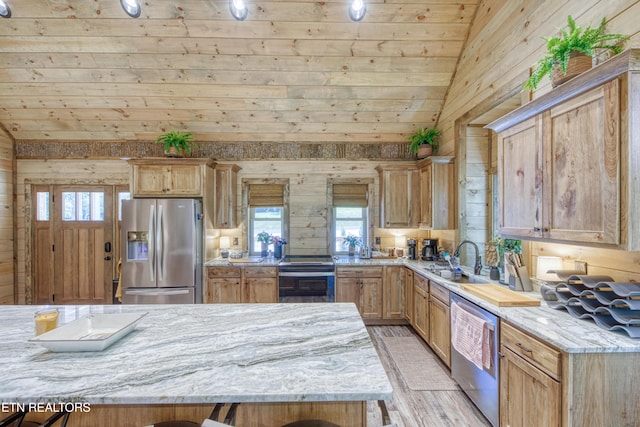 kitchen with lofted ceiling, wooden walls, a sink, appliances with stainless steel finishes, and light stone countertops