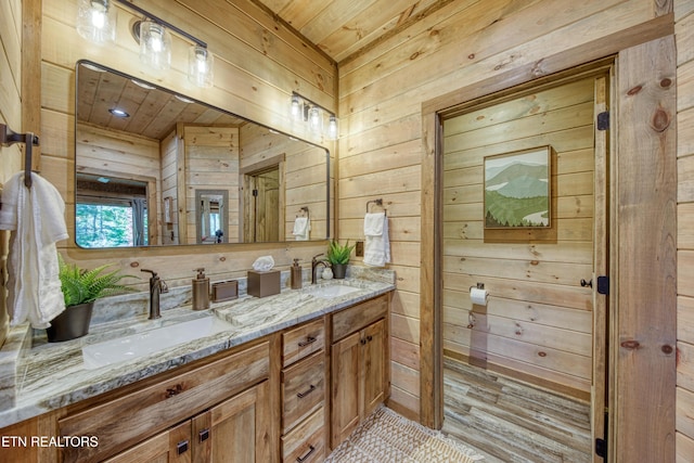 bathroom featuring double vanity, wooden walls, and a sink