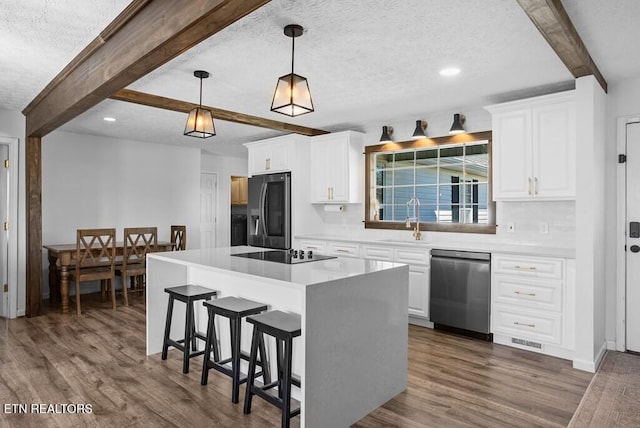 kitchen featuring dark wood-style floors, a breakfast bar, a sink, stainless steel appliances, and beam ceiling