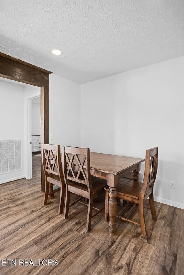 dining room featuring visible vents, a textured ceiling, baseboards, and wood finished floors