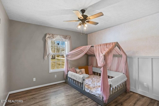 bedroom featuring a ceiling fan, wainscoting, a textured ceiling, and wood finished floors