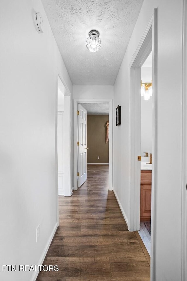 hall with a textured ceiling, dark wood finished floors, and baseboards