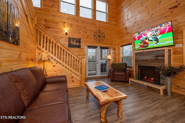 living room featuring wood walls, a fireplace, wood finished floors, a towering ceiling, and stairs