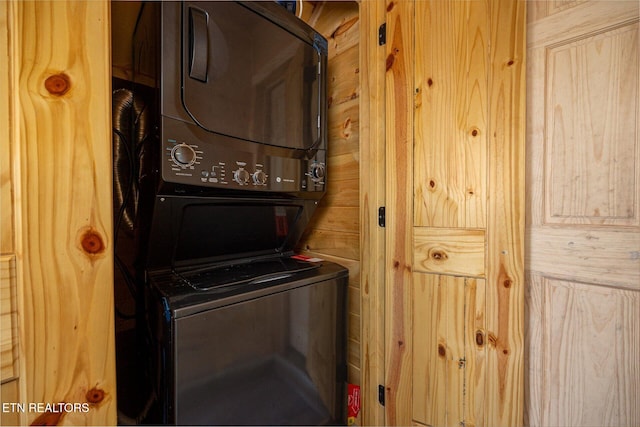 clothes washing area featuring stacked washer and clothes dryer, wood walls, and laundry area