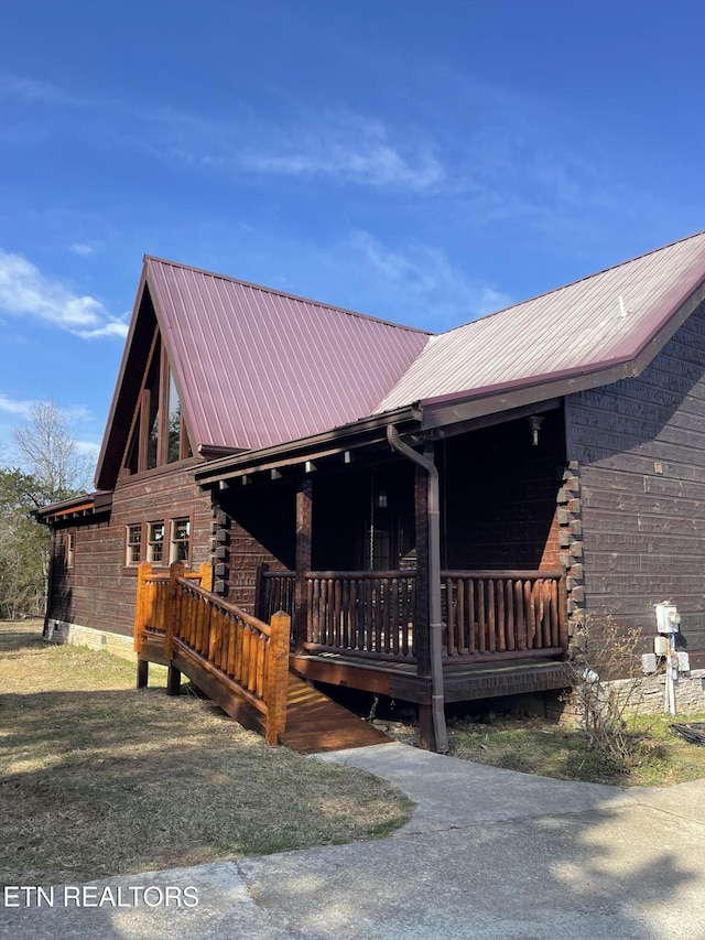 log cabin featuring covered porch, log siding, and metal roof