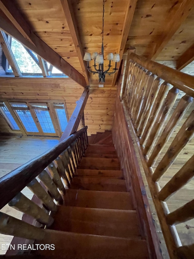 stairs with wooden ceiling, a notable chandelier, wooden walls, wood finished floors, and beamed ceiling