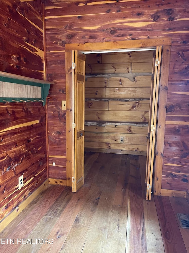 corridor with hardwood / wood-style floors, visible vents, and wooden walls