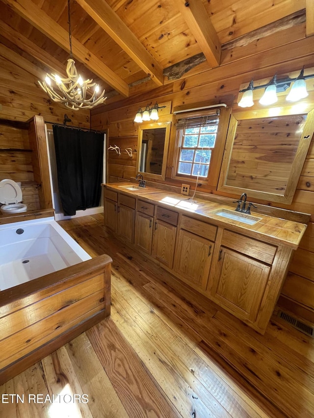 bathroom featuring hardwood / wood-style flooring, wooden walls, visible vents, and a sink