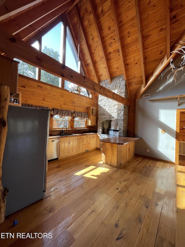 kitchen with a fireplace, appliances with stainless steel finishes, light wood-type flooring, beam ceiling, and dark countertops