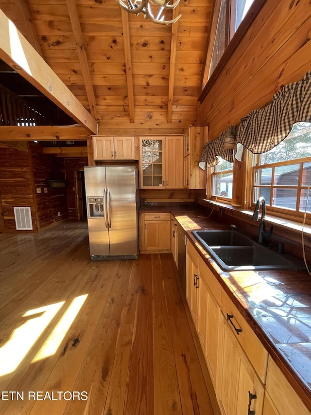 kitchen featuring stainless steel refrigerator with ice dispenser, a sink, wooden walls, beamed ceiling, and hardwood / wood-style floors