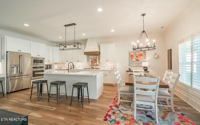 kitchen with stainless steel appliances, a breakfast bar area, premium range hood, and light wood finished floors