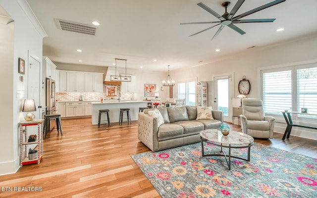 living area with recessed lighting, visible vents, ornamental molding, light wood-type flooring, and ceiling fan with notable chandelier