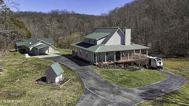 view of front of home with an outbuilding, a porch, a front lawn, a chimney, and a view of trees