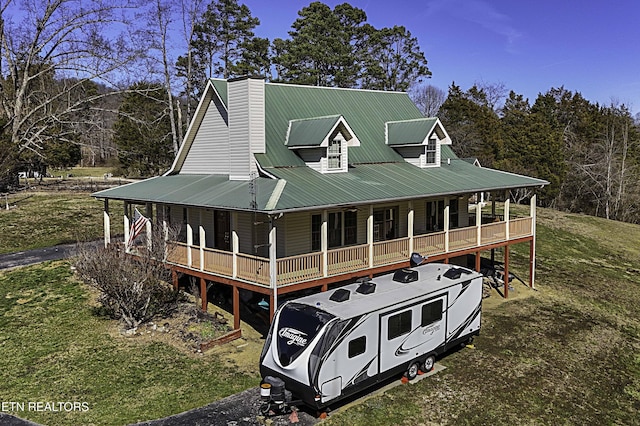 farmhouse-style home featuring covered porch, a chimney, metal roof, and a front yard