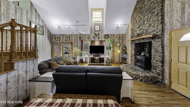 living area featuring a textured ceiling, high vaulted ceiling, wood finished floors, a ceiling fan, and a wood stove