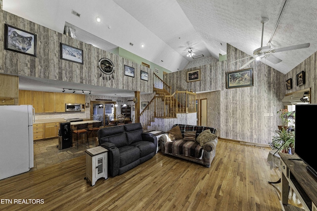 living area with a ceiling fan, wood finished floors, high vaulted ceiling, and stairs