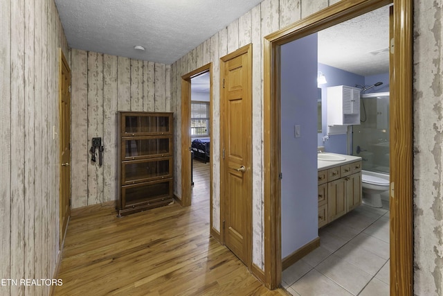 hallway with a textured ceiling, a sink, light wood-style flooring, and wallpapered walls