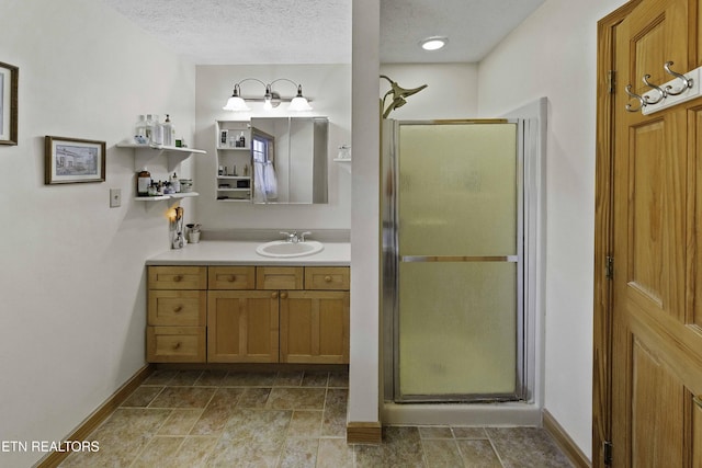 bathroom featuring a textured ceiling, a shower stall, vanity, and baseboards