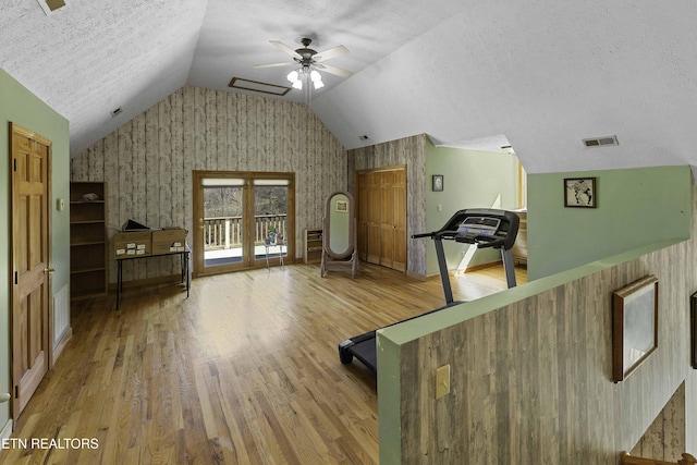 workout area with a textured ceiling, wood finished floors, visible vents, a ceiling fan, and vaulted ceiling