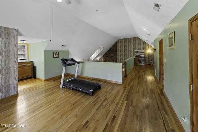 workout area with lofted ceiling, visible vents, baseboards, and wood finished floors