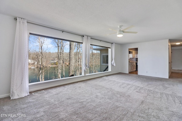 carpeted empty room featuring a ceiling fan, visible vents, and a textured ceiling