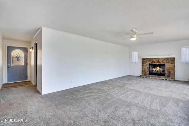 unfurnished living room with carpet floors, a textured ceiling, a ceiling fan, and a stone fireplace