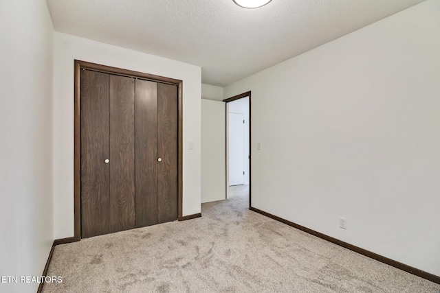 unfurnished bedroom featuring carpet floors, a textured ceiling, baseboards, and a closet