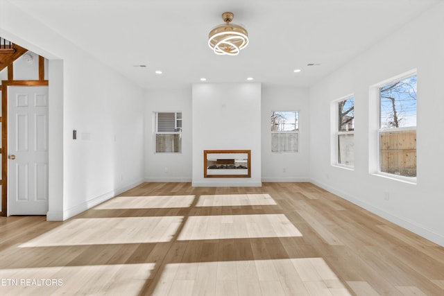 unfurnished living room with light wood-style floors, a wealth of natural light, a glass covered fireplace, and recessed lighting