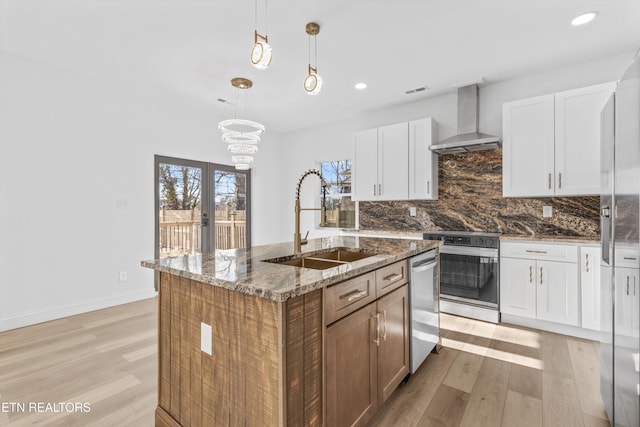 kitchen with an island with sink, a sink, stainless steel appliances, wall chimney range hood, and backsplash