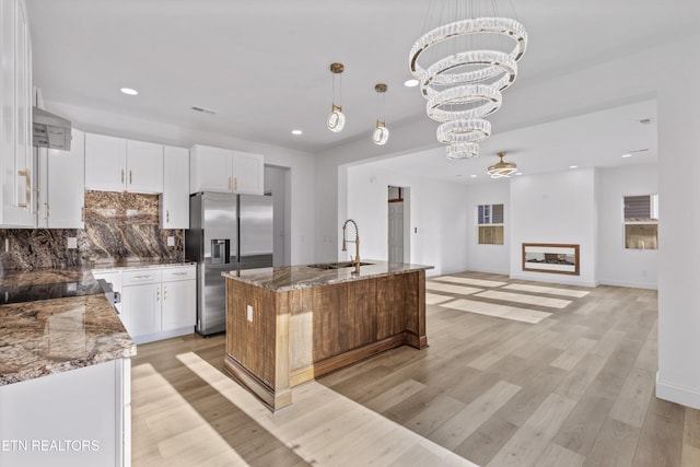 kitchen featuring tasteful backsplash, stainless steel fridge, light wood-style flooring, stone counters, and a sink