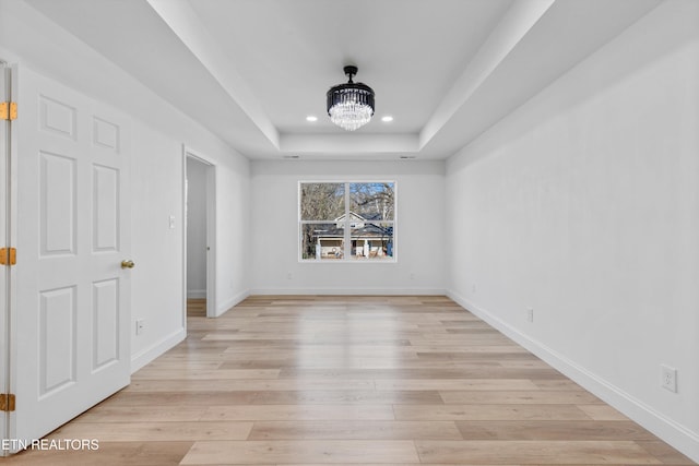 unfurnished room featuring light wood-style floors, a tray ceiling, a notable chandelier, and baseboards