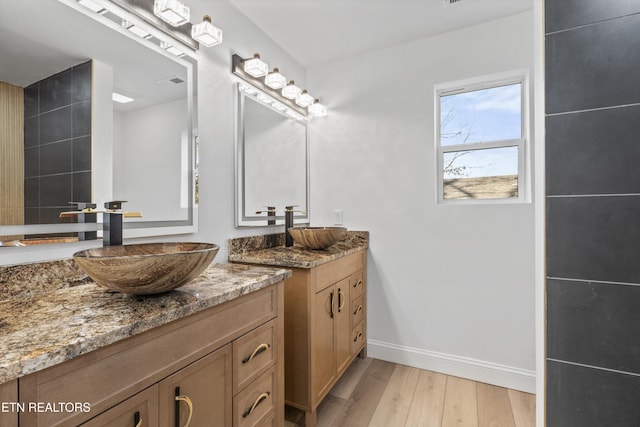 full bathroom featuring wood finished floors, two vanities, a sink, and baseboards