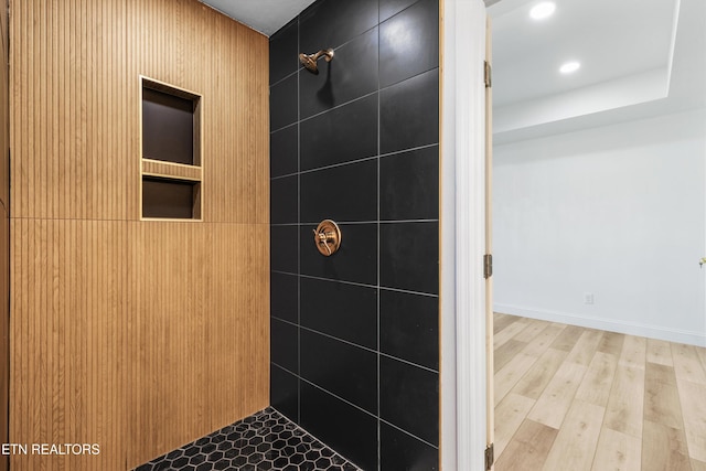 bathroom featuring baseboards, a tile shower, wood finished floors, and recessed lighting