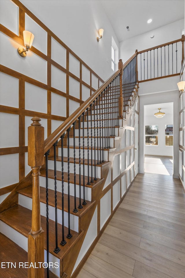 staircase with a towering ceiling, plenty of natural light, wood finished floors, and recessed lighting