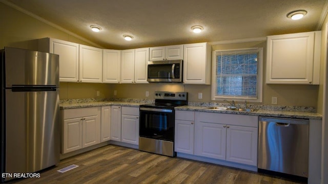 kitchen featuring appliances with stainless steel finishes, white cabinetry, vaulted ceiling, a sink, and a textured ceiling