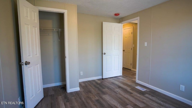 unfurnished bedroom featuring a closet, dark wood finished floors, a textured ceiling, and baseboards