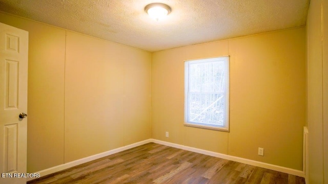 spare room with a wealth of natural light, a textured ceiling, baseboards, and wood finished floors