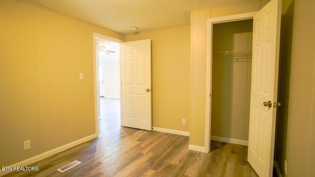 unfurnished bedroom with a closet, visible vents, a textured ceiling, wood finished floors, and baseboards