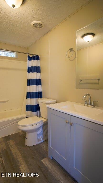 bathroom with a textured ceiling, toilet, wood finished floors, vanity, and shower / bathtub combination with curtain