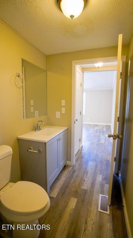 half bathroom featuring a textured ceiling, toilet, wood finished floors, and visible vents