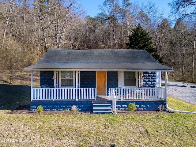 view of front facade featuring covered porch, a front yard, and a view of trees