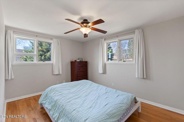 bedroom with multiple windows, wood finished floors, and baseboards