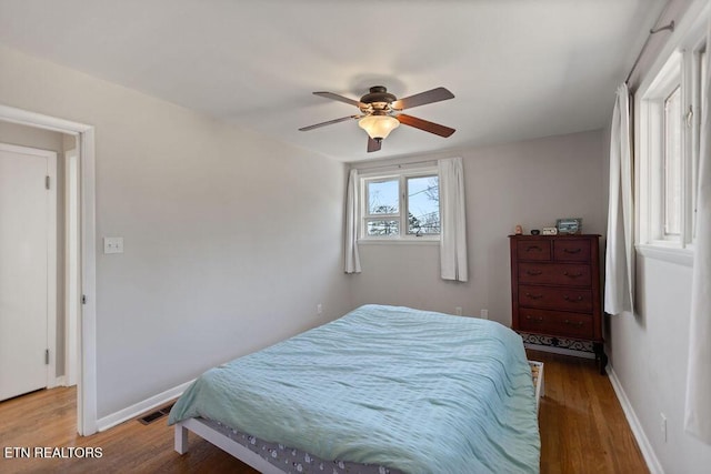 bedroom featuring ceiling fan, visible vents, baseboards, and wood finished floors