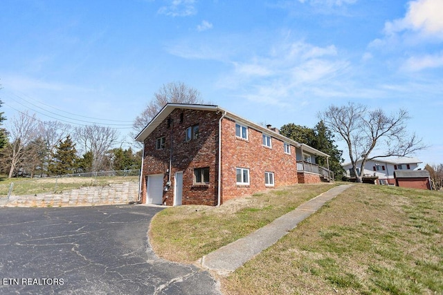 view of property exterior with driveway, fence, a yard, an attached garage, and brick siding