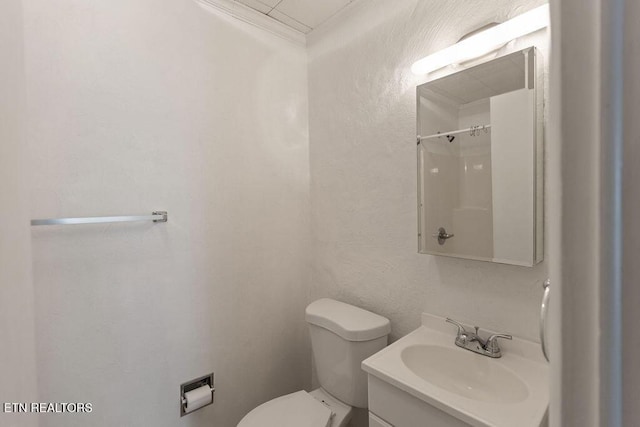 bathroom featuring toilet, vanity, a textured wall, and ornamental molding