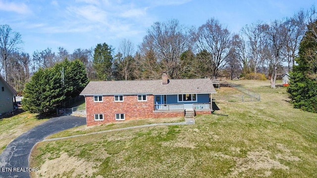 ranch-style house featuring aphalt driveway, a chimney, a front yard, and brick siding