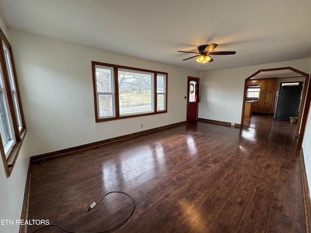 empty room with arched walkways, dark wood-style flooring, and a healthy amount of sunlight