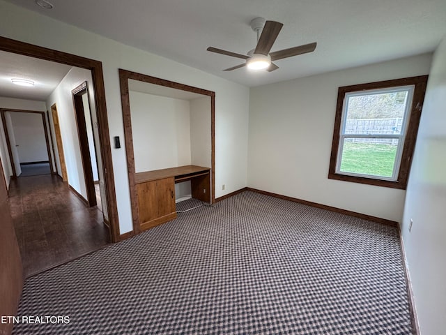 carpeted spare room featuring built in desk, a ceiling fan, and baseboards