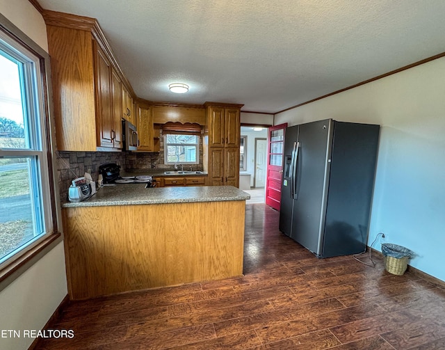 kitchen featuring brown cabinetry, dark wood finished floors, a peninsula, stainless steel appliances, and a sink