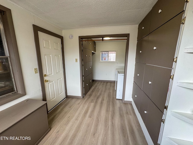 hallway featuring washer / clothes dryer, baseboards, light wood-style flooring, and a textured ceiling